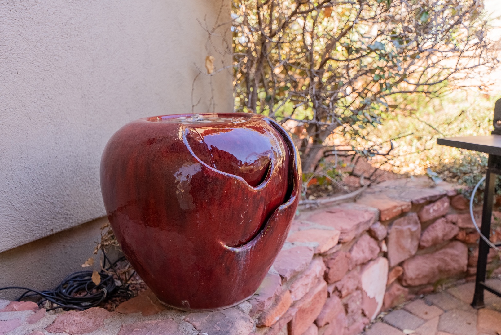A stunning red ceramic water feature adds artistic charm to your private patio, surrounded by natural stone and autumn foliage.