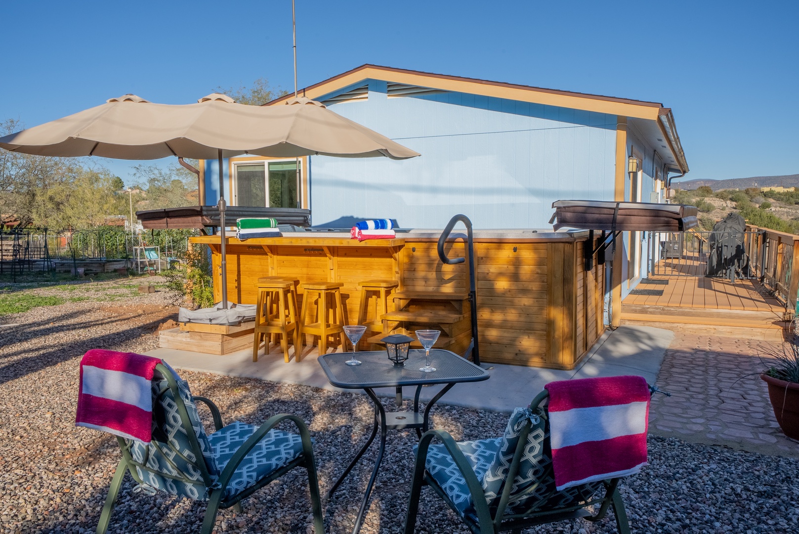 Modern property with outdoor hot tub, bar seating area, and patio space surrounded by natural desert landscape under clear blue skies.