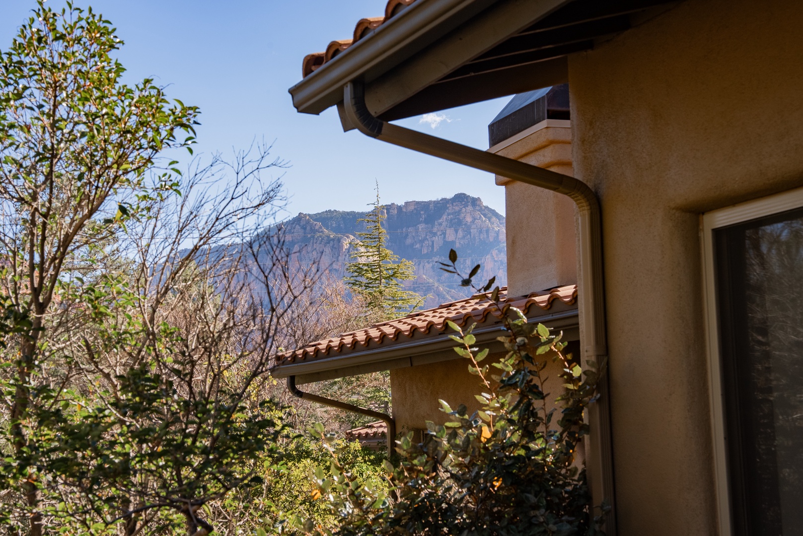 Mediterranean-style property nestled among mature trees with dramatic mountain backdrop creating a serene desert setting.