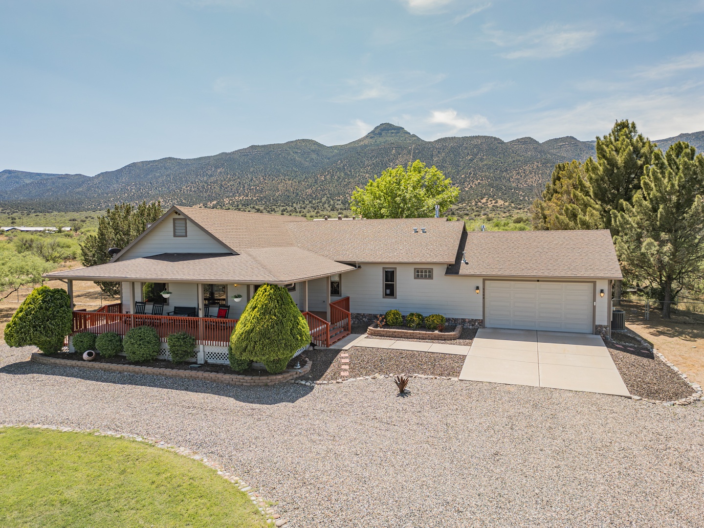 Single-story vacation home with wrap-around porch nestled against scenic mountain backdrop, offering peaceful desert valley retreat.