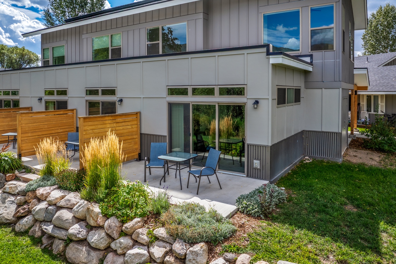 This modern townhome has an exterior featuring a private patio that backs up to the river with dining area, decorative landscaping, and contemporary architectural design.