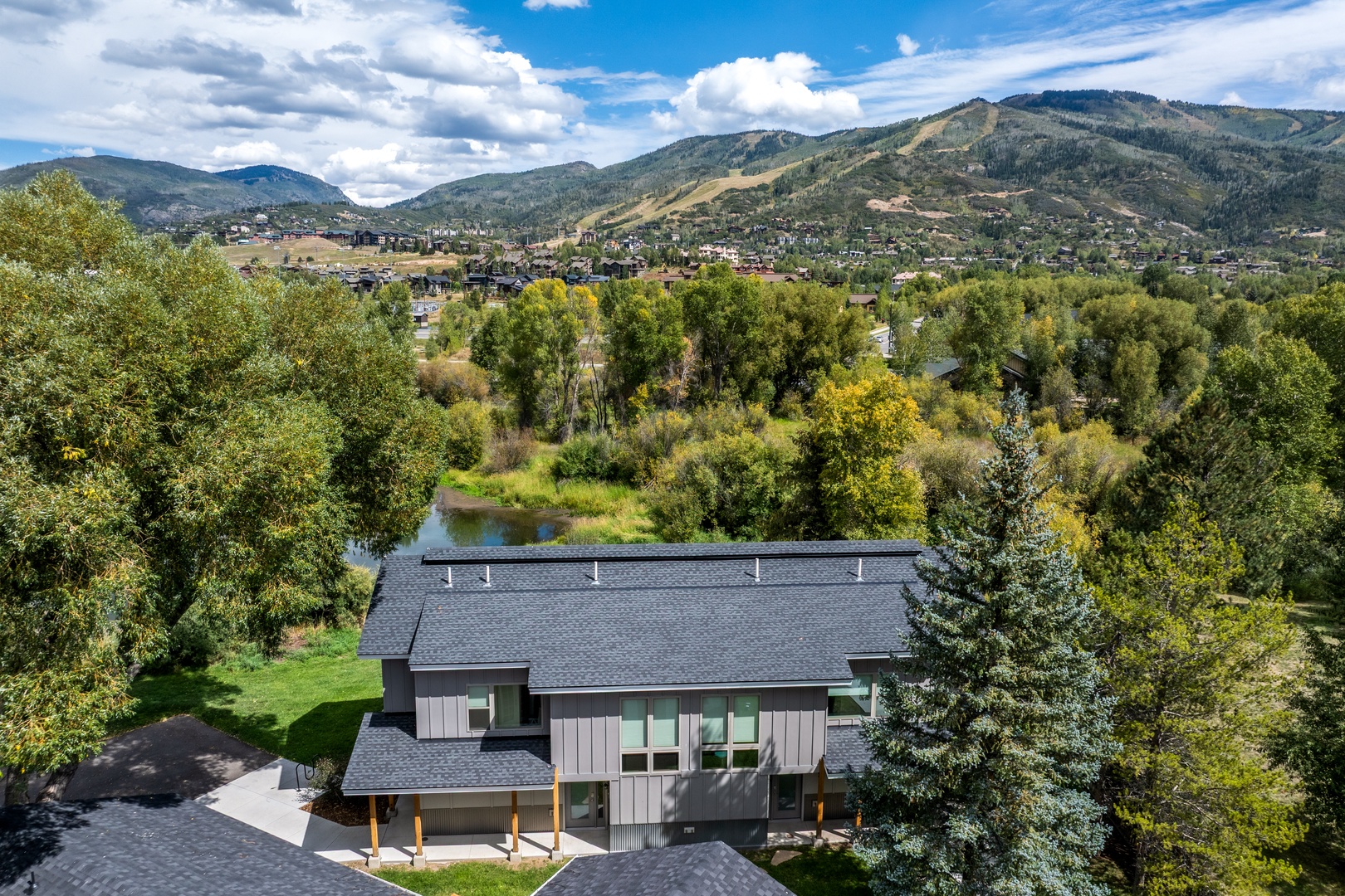 Aerial view showcasing the property nestled in a scenic mountain valley with a tranquil river, surrounded by lush trees and expansive natural beauty in the surrounding area.