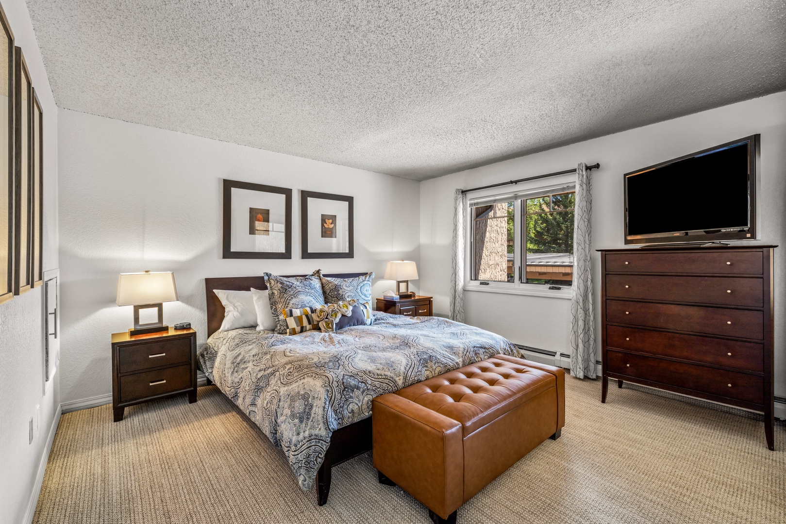 The lower level unit has a plush queen bed, with elegant dark wood furnishings, a large flat-screen TV, and serene wooded views creating your perfect alpine retreat.