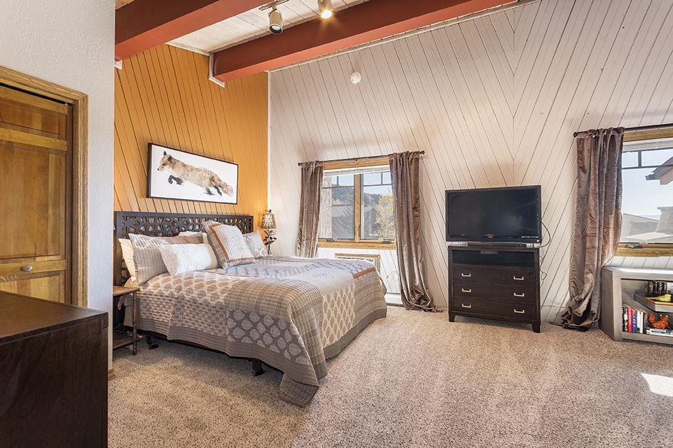 Sink into your plush king bed beneath vaulted wood ceilings, where natural light streams through multiple windows and the mountain-chic décor sets a cozy, relaxed tone.