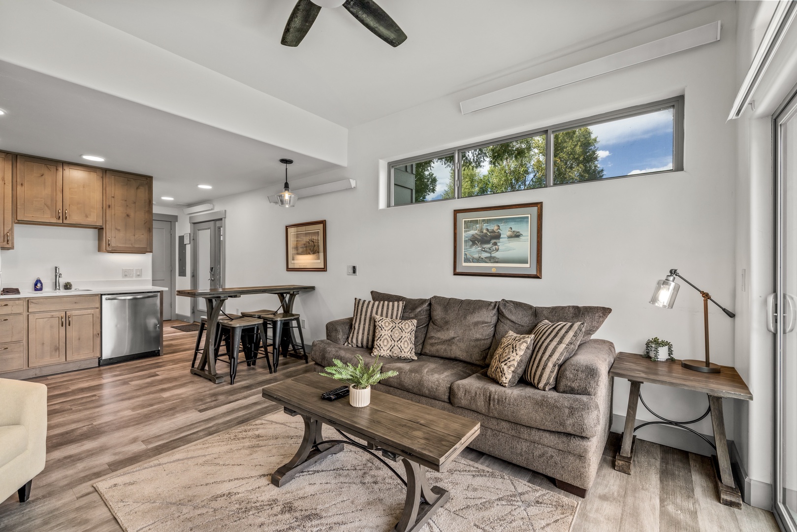Relax in your bright, open-plan retreat where rustic wood meets modern comfort. Natural light pours through tall windows, highlighting the cozy living area and fully equipped kitchen—your perfect home base for unwinding after adventure.