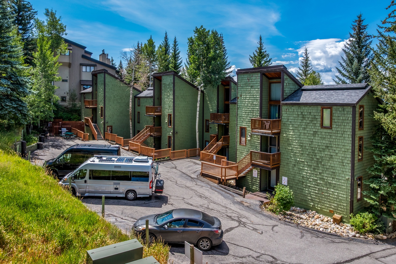 Forest-framed mountain lodging with private balconies, warm wood accents, and parking nestled among evergreens under open alpine skies.