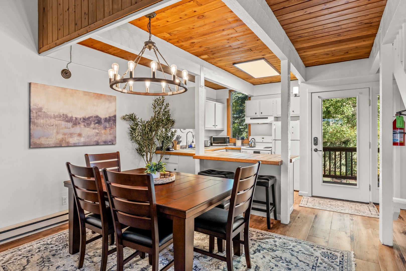 Gather around the warm wood dining table beneath soaring ceilings, where natural light pours in through the open door and greenery beckons just beyond your retreat.
