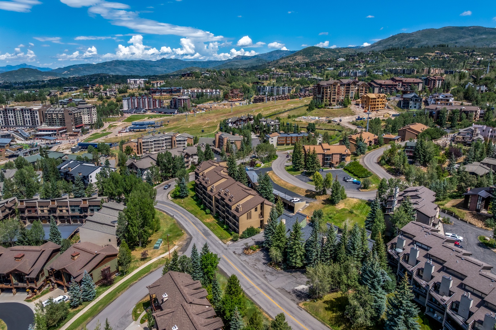 An aerial view showcasing the property nestled within a scenic mountain valley community, surrounded by forested slopes and neighboring vacation homes.