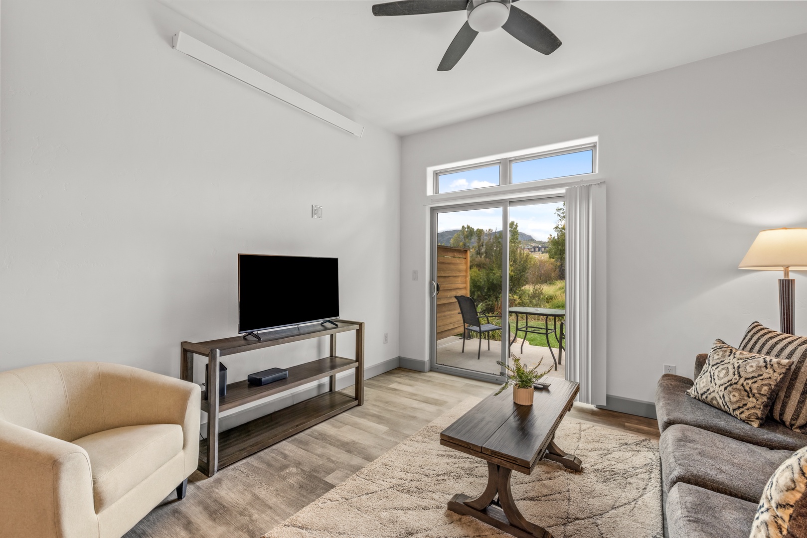 Unwind in your bright, open living room where sunlight spills through tall windows and a ceiling fan keeps you comfortable. Step outside to your private patio and take in peaceful mountain views framed by trees and greenery.