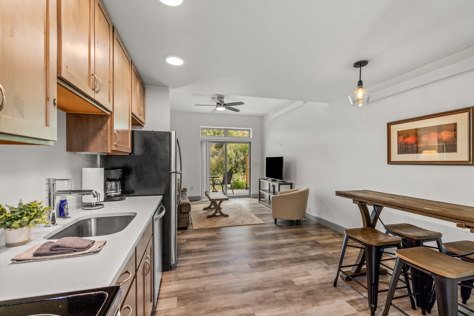 Your open-plan living space flows seamlessly from kitchen to dining to lounge, with warm wood accents and natural light streaming through glass doors that open to a peaceful garden view.