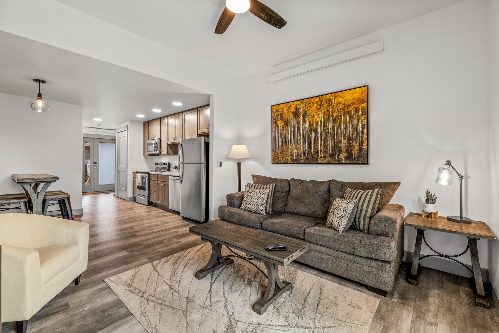 Open and inviting, your living area flows seamlessly into a fully equipped kitchen with modern appliances and wood-toned cabinetry. High ceilings and warm lighting create a welcoming retreat.