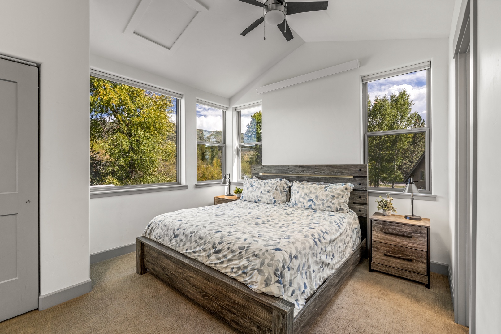 Wake up to nature's beauty in this tranquil bedroom, where three large windows frame lush treetops and mountains. The ceiling fan keeps your space comfortable while you enjoy peaceful surroundings.