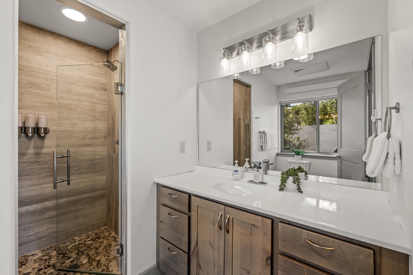Step into your spa-like bathroom featuring a sleek walk-in shower with warm wood-grain tile, a bright vanity, and modern lighting—your personal retreat awaits.