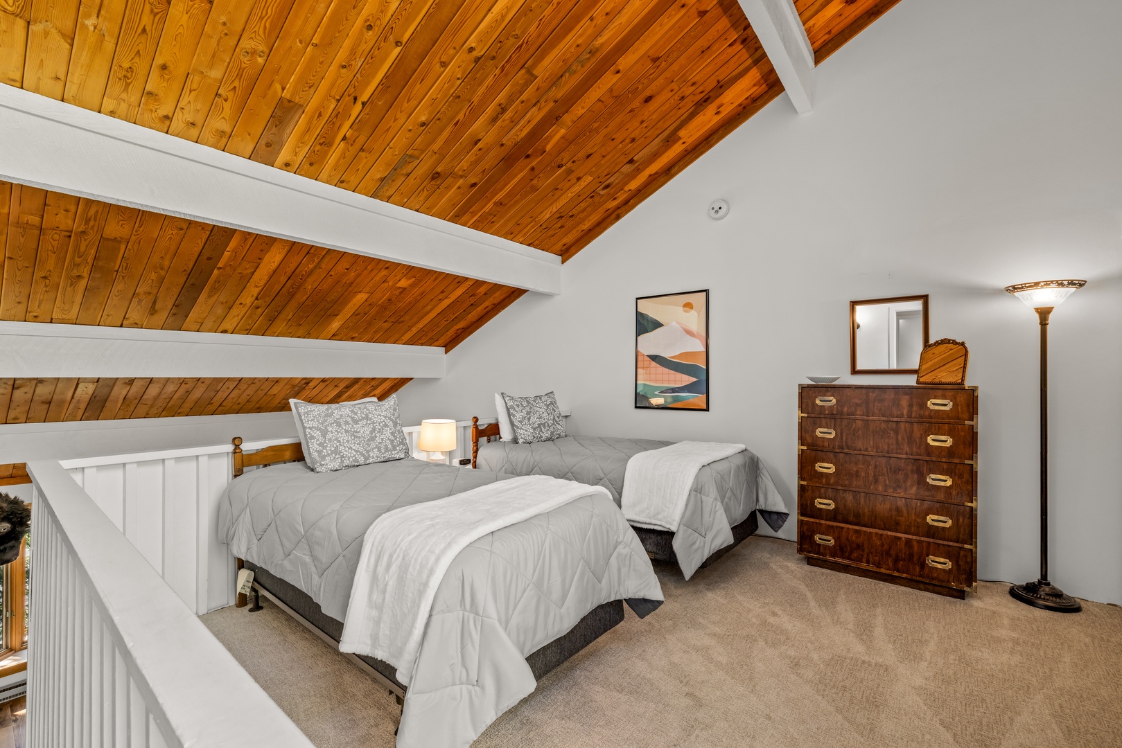 Unwind in your charming loft bedroom with vaulted wood-plank ceilings that create a cozy, cabin-inspired retreat. Two twin beds invite restful nights under warm ambient lighting.