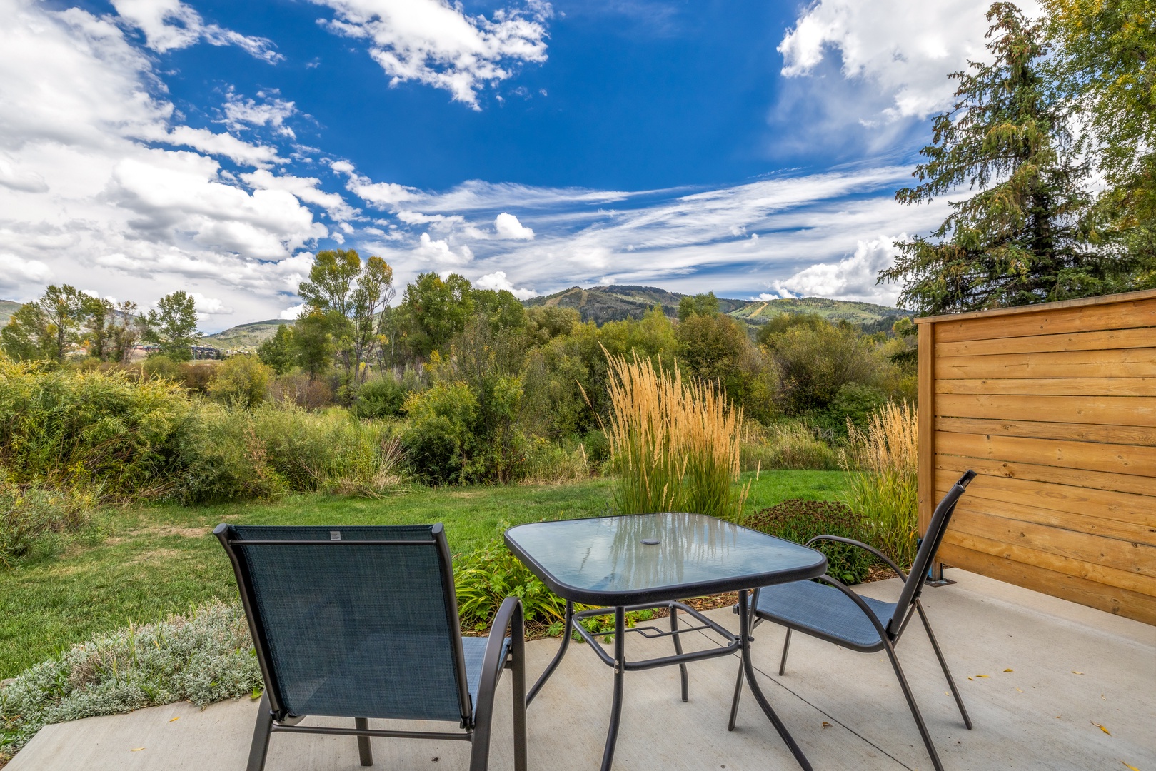 A peaceful outdoor patio surrounded by rolling hills and natural landscaping, framed by a wooden privacy fence that creates a serene backdrop for morning coffee or evening relaxation.