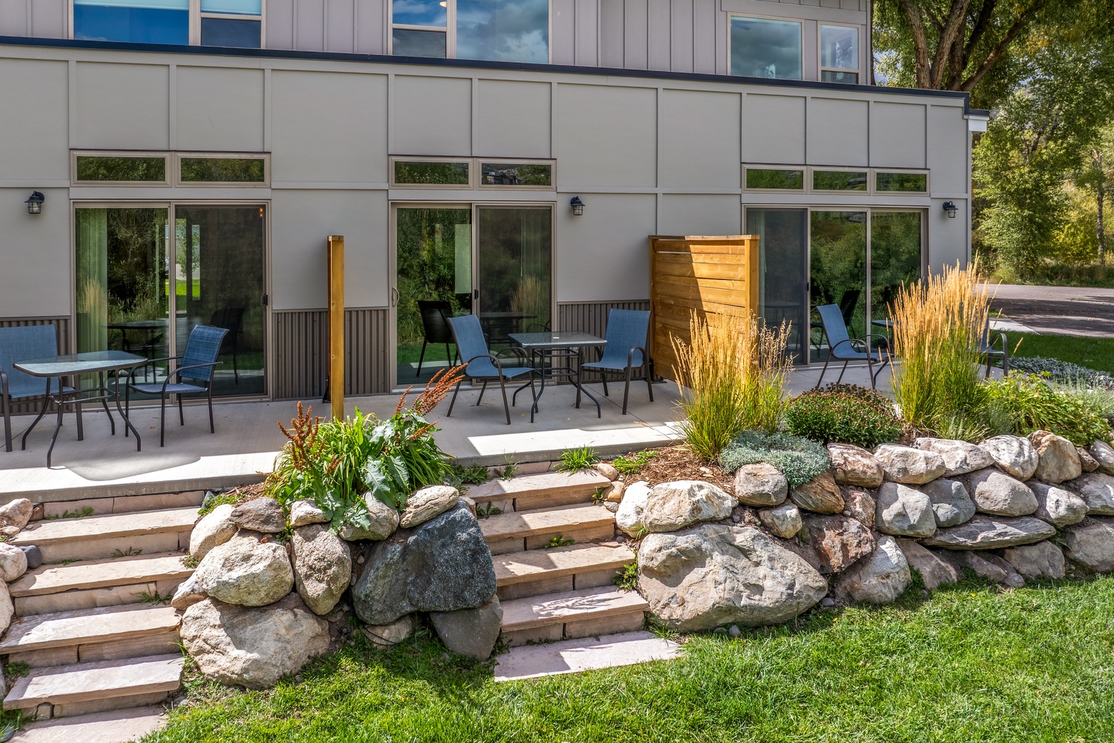 Modern vacation rental exterior featuring a landscaped garden and spacious patio area with multiple seating spaces for outdoor dining and relaxation.
