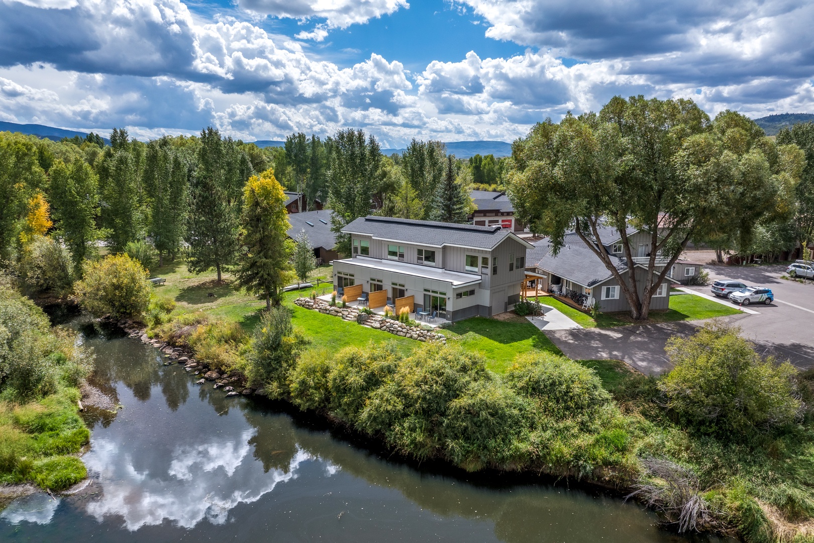 Modern vacation rental nestled along a peaceful riverside, surrounded by lush trees and distant mountain vistas.