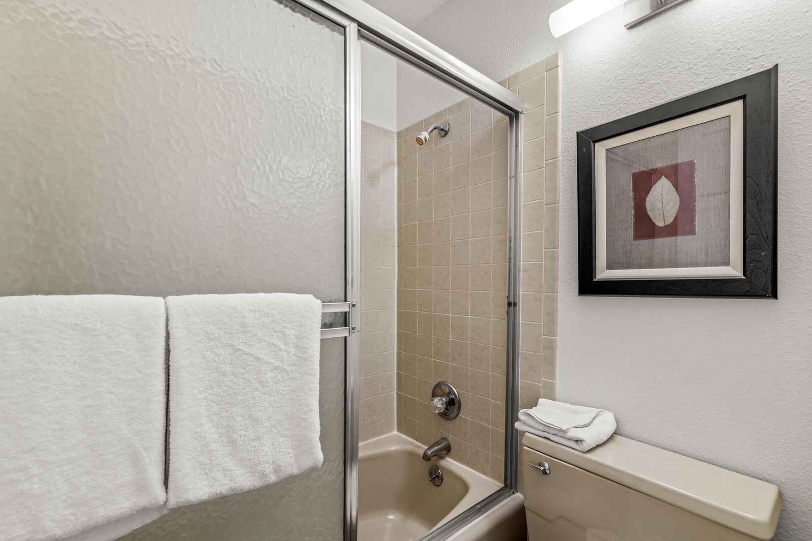 Step into your private bathroom featuring a tiled shower-tub combo with a sliding glass door, fluffy white towels, and a soothing neutral palette.