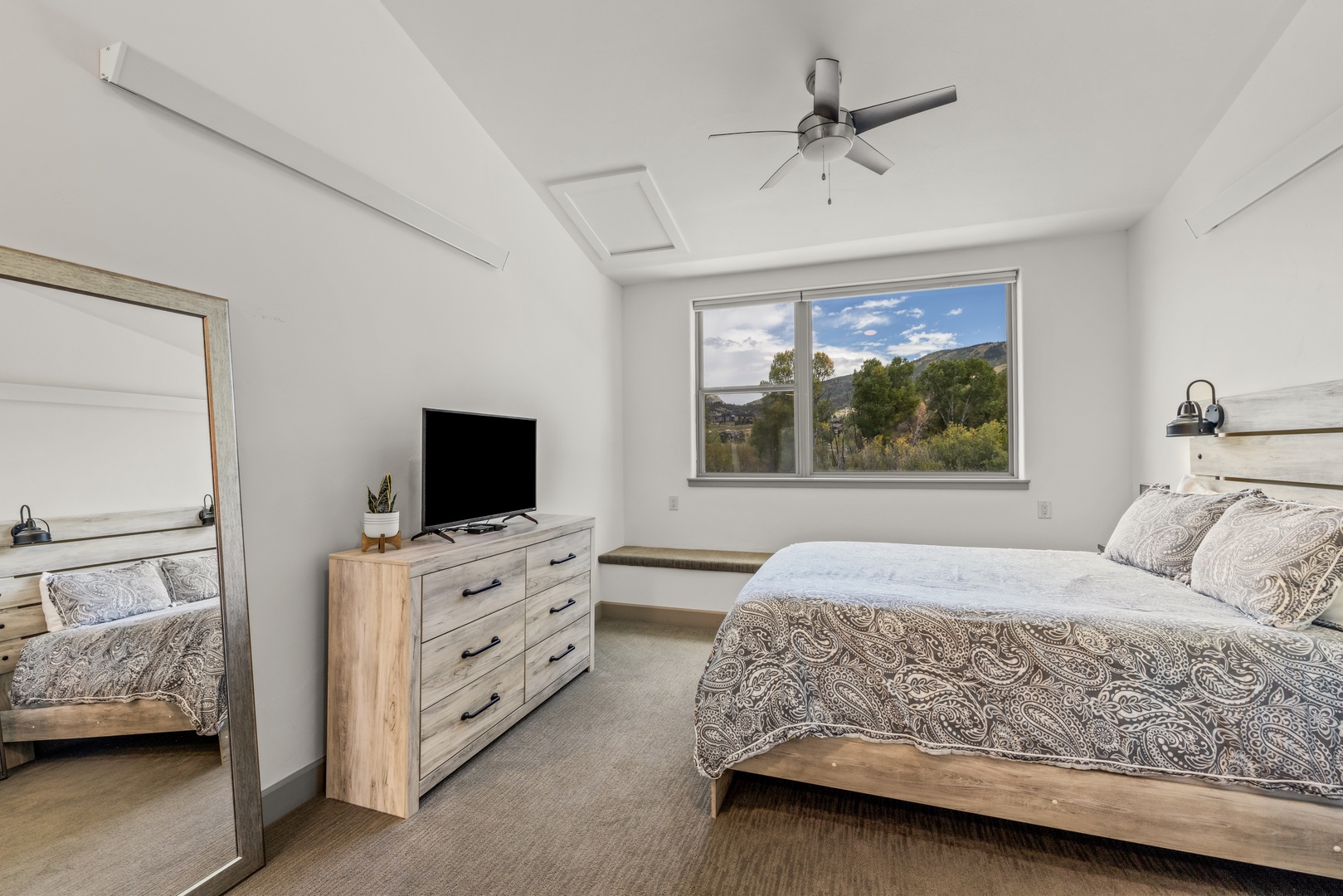 Drift off in your serene bedroom, where crisp white walls and warm wood tones create a peaceful retreat. Natural light and mountain views through the window make this your perfect sanctuary.