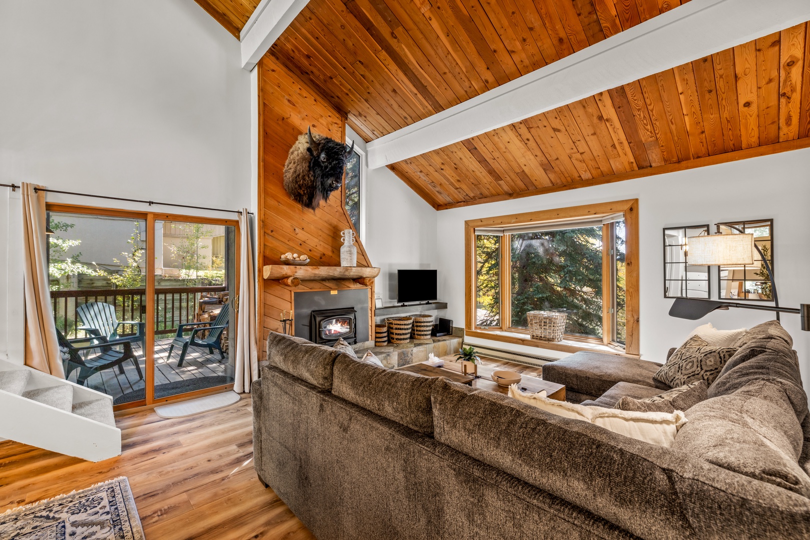 Sink into plush seating beneath soaring wood-beamed ceilings, where your cozy fireplace sets the mood for mountain evenings and large windows frame the forest beyond.