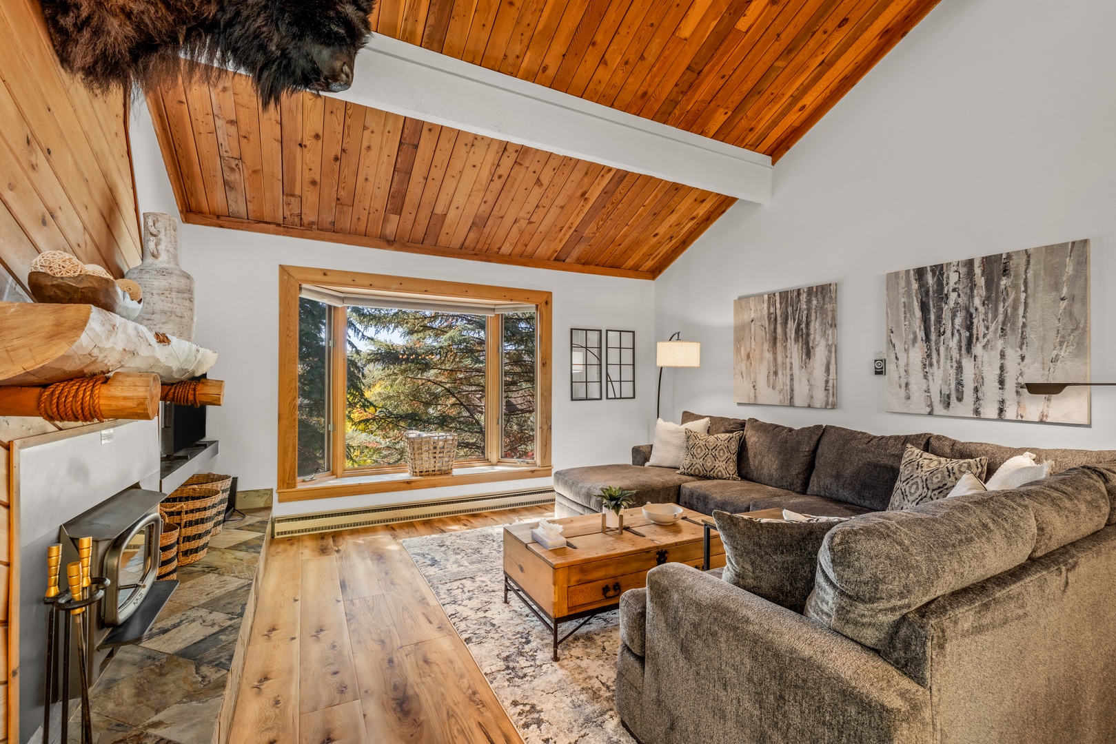 Unwind in your cozy living room with soaring wood ceilings, plush seating, and a crackling fireplace—mountain views framed perfectly through the picture window.