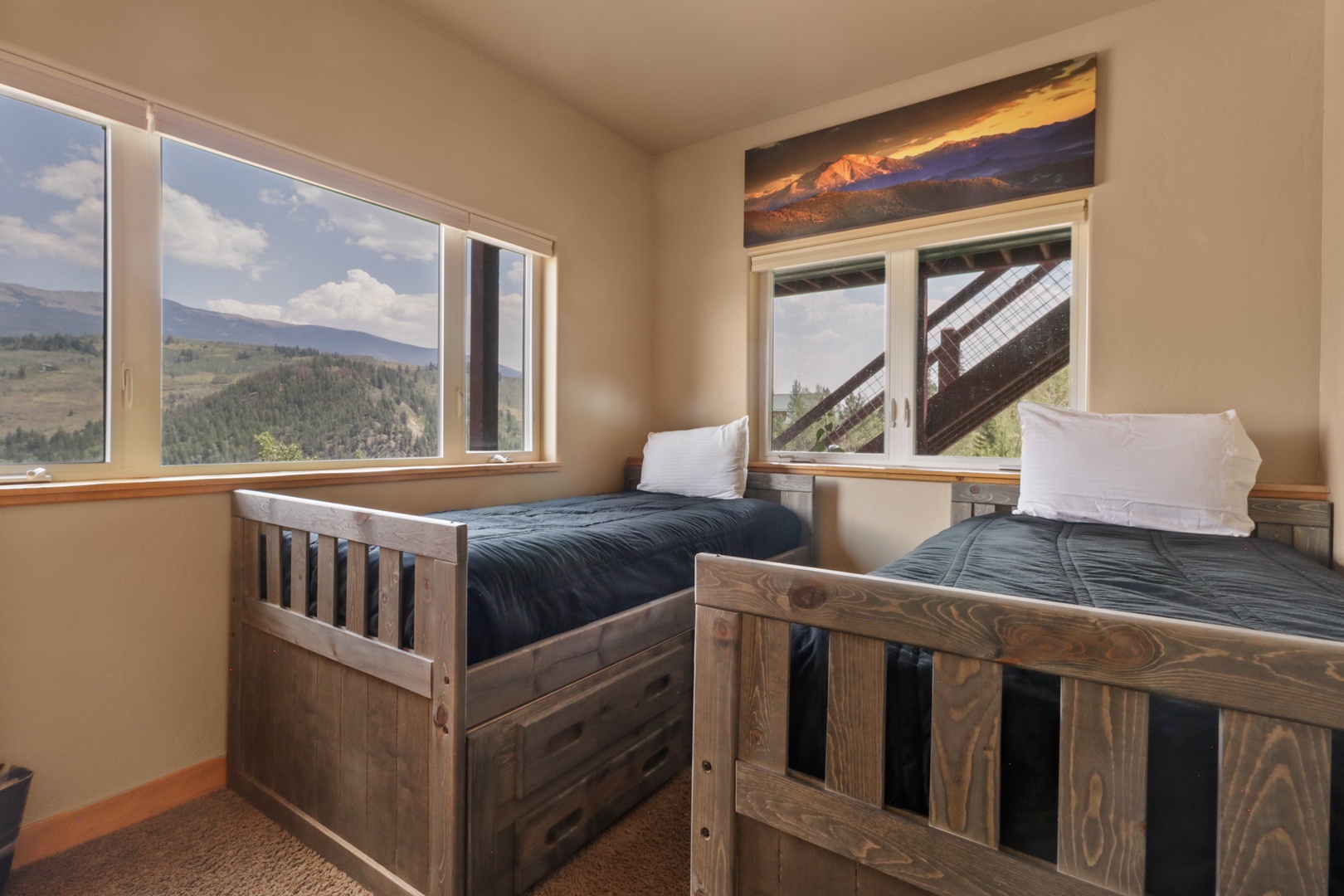 Your cozy room features twin beds with rustic wooden frames, fresh linens, and large windows that frame stunning mountain vistas—the perfect retreat after a day of exploring.