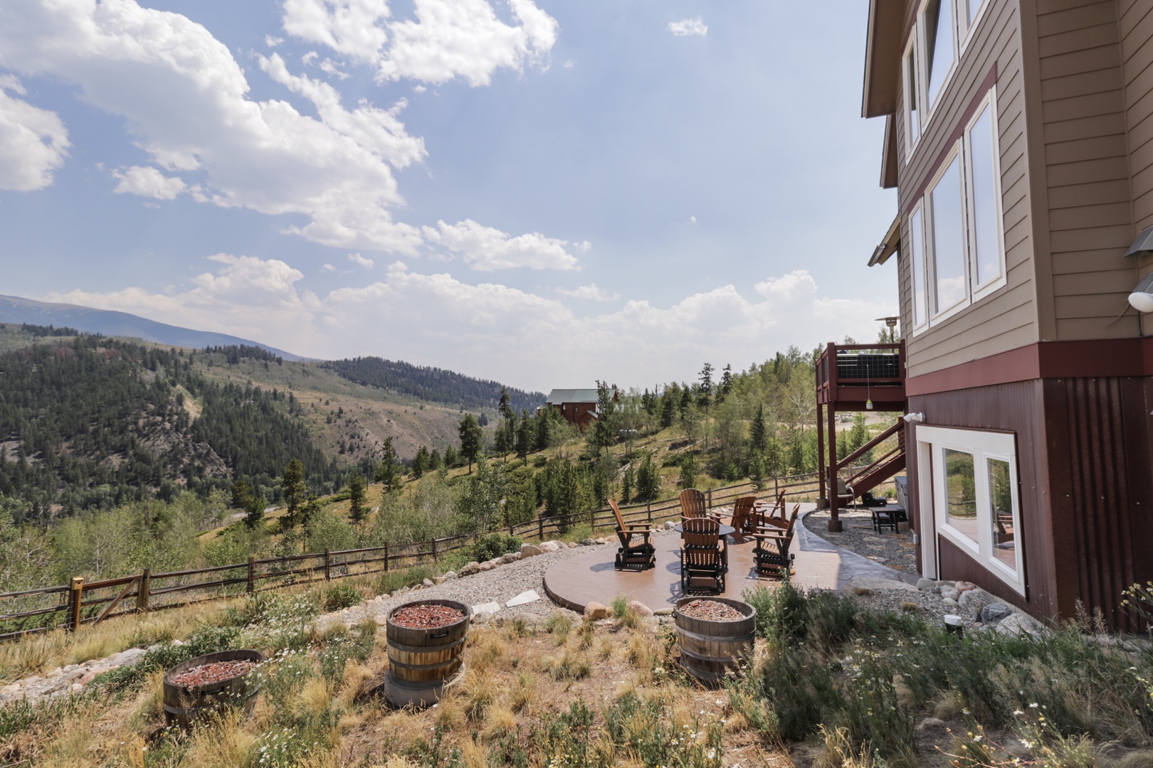 This mountain retreat features a scenic patio with rustic seating surrounded by natural landscaping, set against a backdrop of forested hillsides and expansive sky—an ideal setting for peaceful relaxation.
