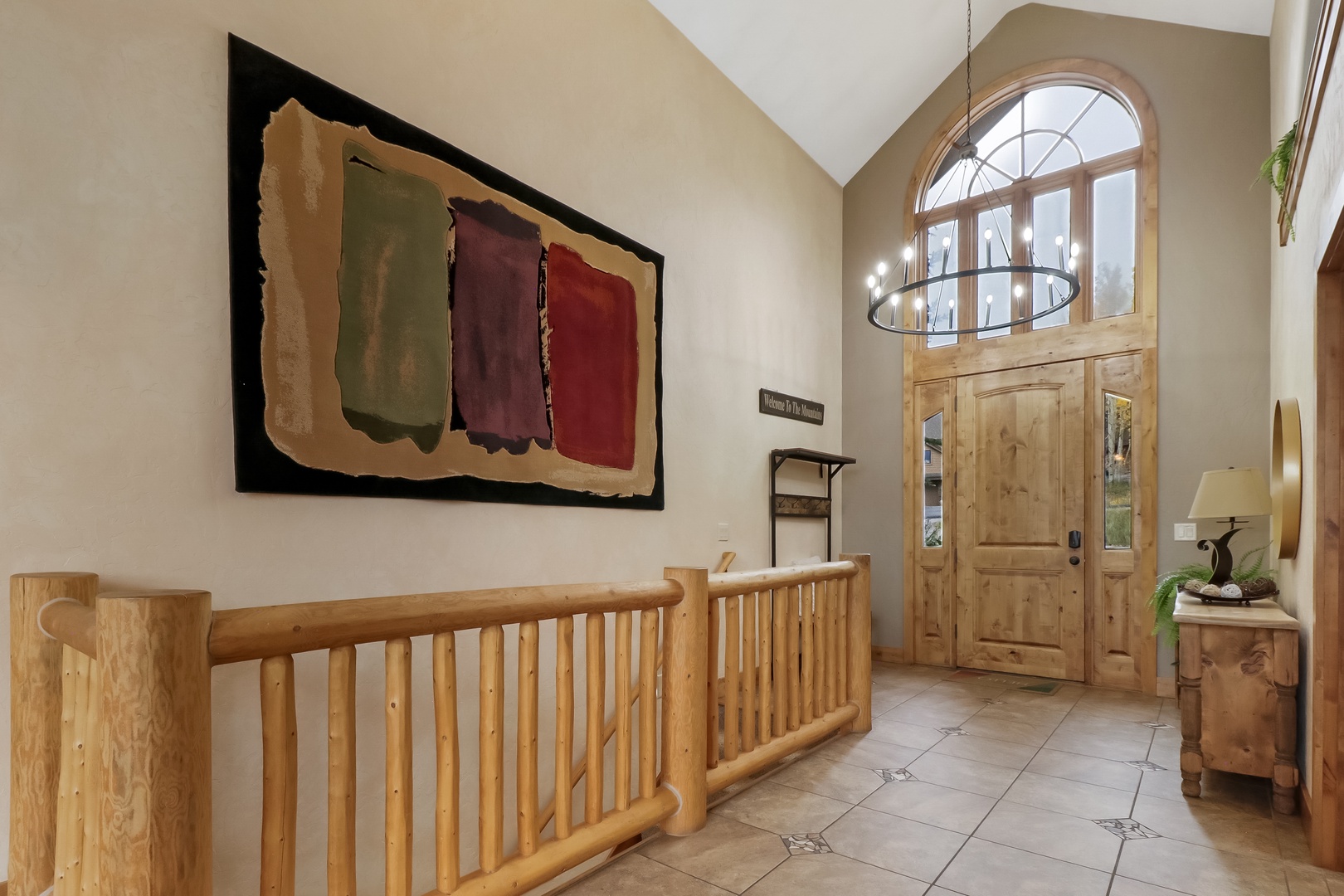 The grand entryway welcomes you with soaring vaulted ceilings, warm natural wood accents, and abundant light streaming through the arched transom window above the door.