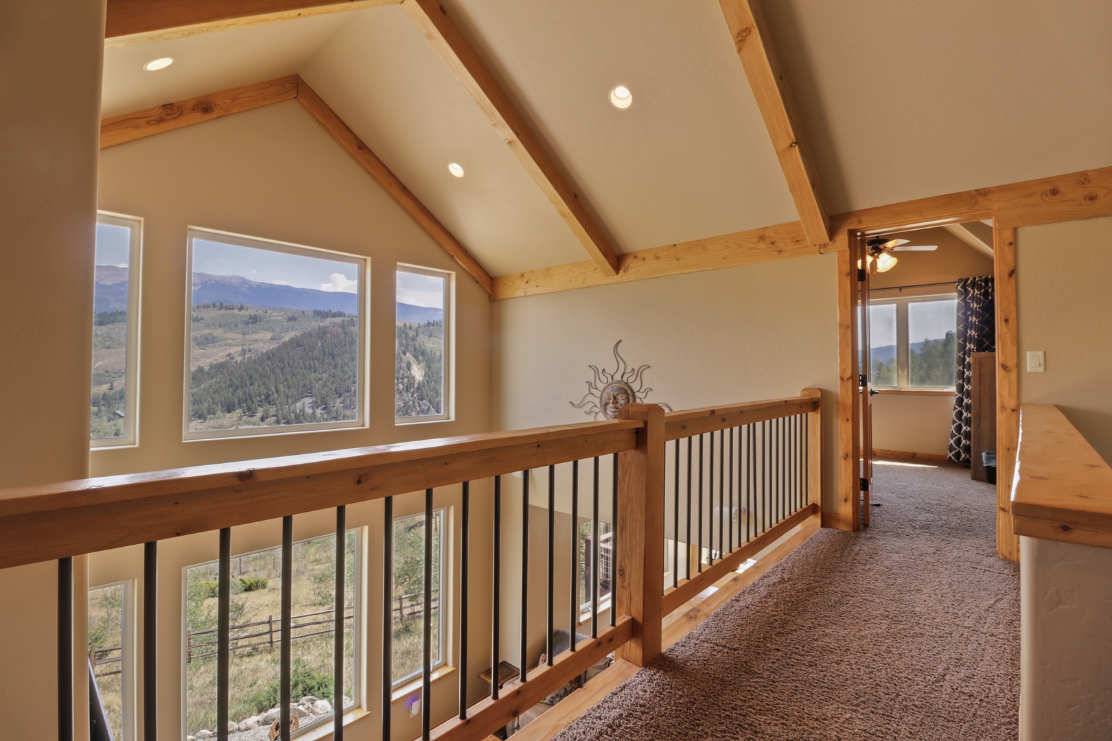 Upper-level loft with soaring vaulted ceilings, exposed beams, and panoramic mountain views from expansive windows. Private balcony included.