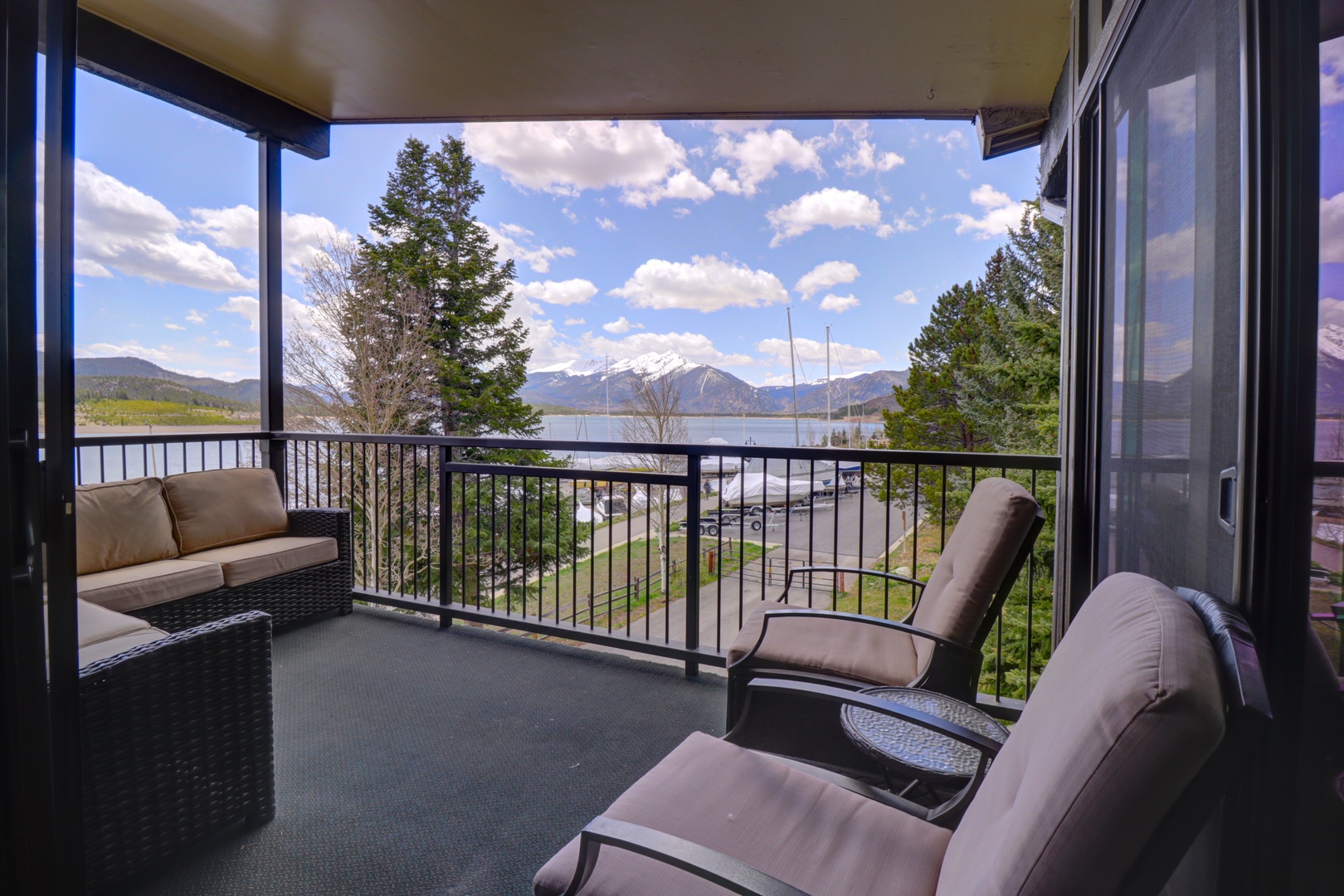 A serene mountain and lake panorama unfolds beyond your private covered balcony, where comfortable outdoor seating invites you to relax and soak in the breathtaking alpine scenery.