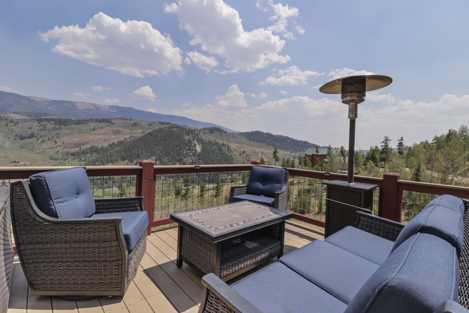 Mountain views stretch across rolling hills and forested ridges, framing this elevated deck where blue skies and fresh air create a peaceful backdrop for outdoor relaxation.