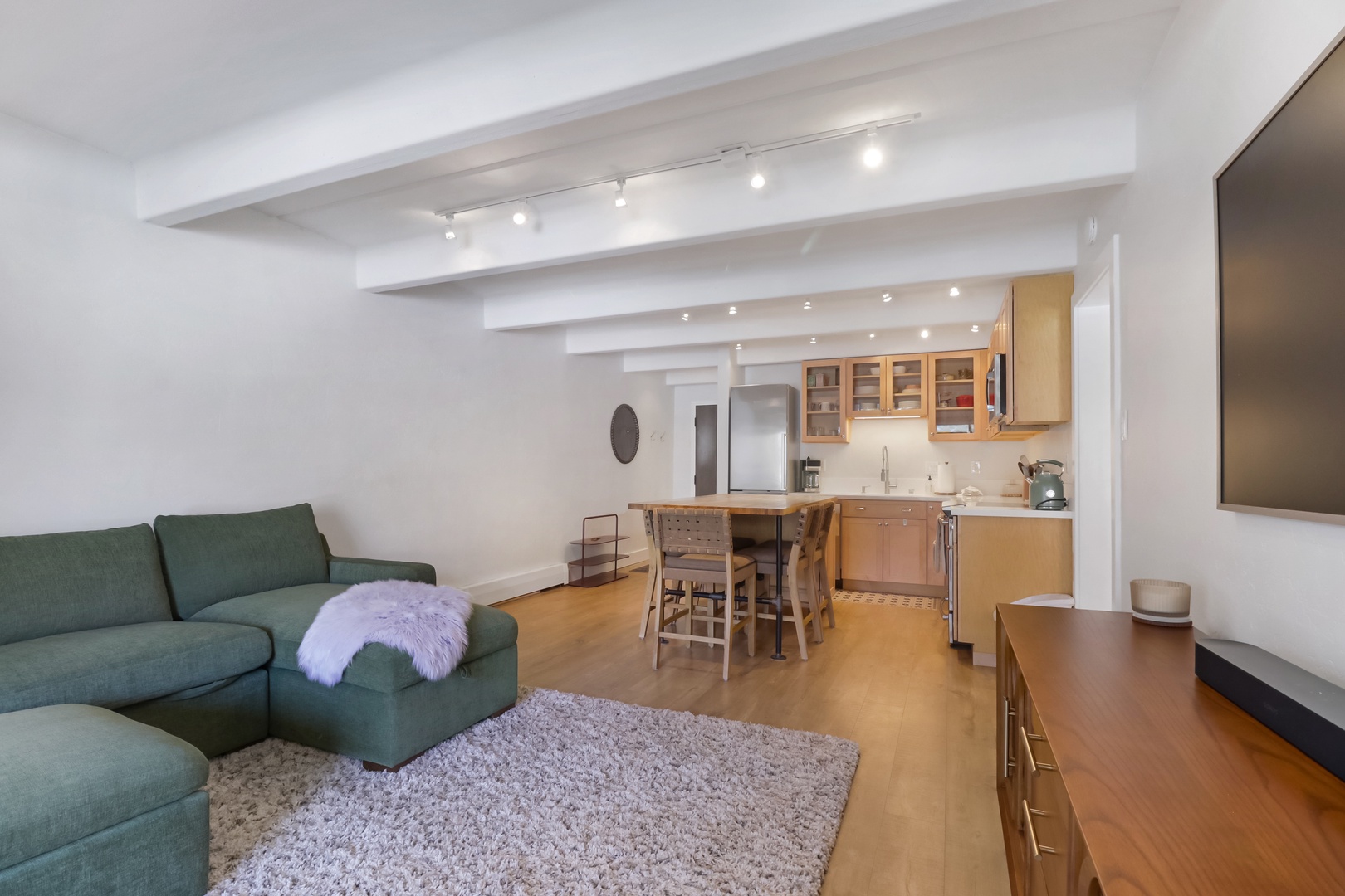 Relax in your bright open-concept space with cozy sofa, fully equipped kitchen, and charming exposed beams creating the perfect home-away-from-home.