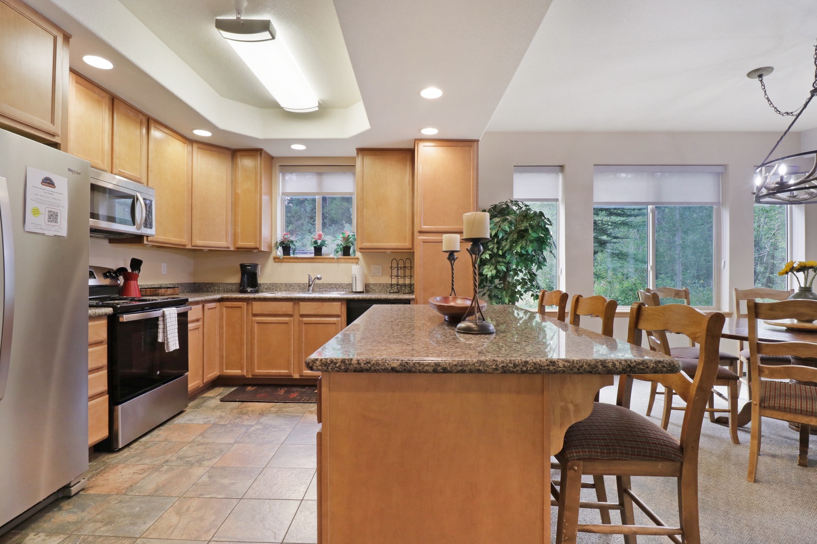 Your spacious kitchen features warm wood cabinetry, granite countertops, and a large island perfect for preparing meals or gathering with loved ones. Natural light pours in through the windows, filling the space with warmth.