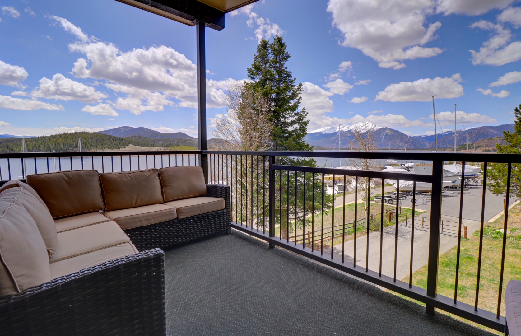 This third-floor covered balcony overlooks a lake and mountain range, featuring outdoor seating for relaxation.
