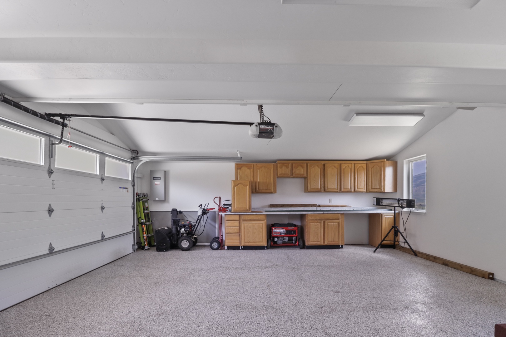 A spacious two-car garage features pristine speckled flooring, honey oak cabinetry with generous counter space, and convenient built-in storage. The organized layout provides ample room for both parking and projects.