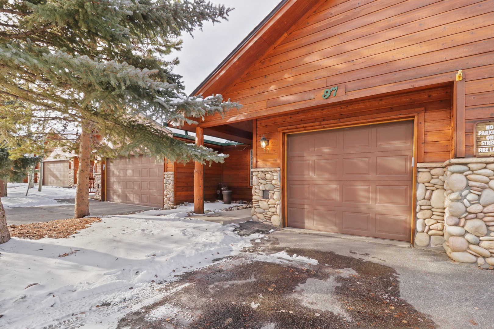 Charming mountain lodge featuring warm wood and stone architecture with convenient garage access and winter mountain setting.