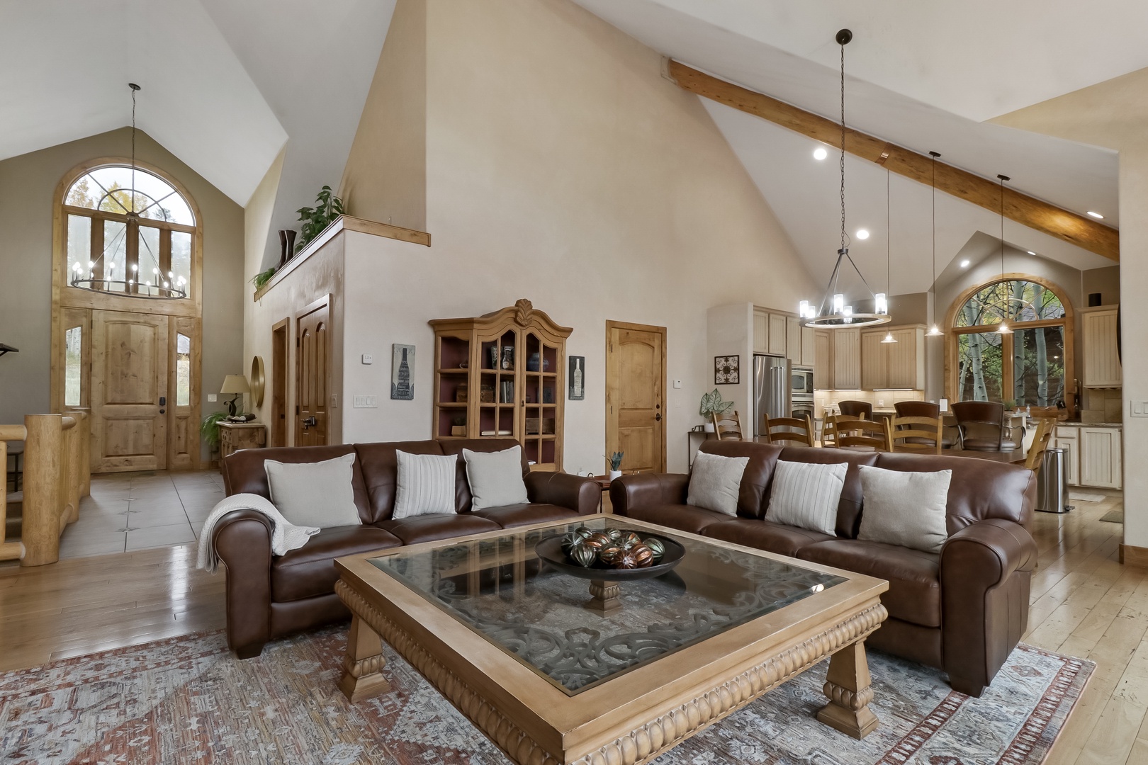 Bright, open-concept retreat with vaulted ceilings, warm wood beams, plush leather sofas, and elegant arched windows flooding the space with natural light.