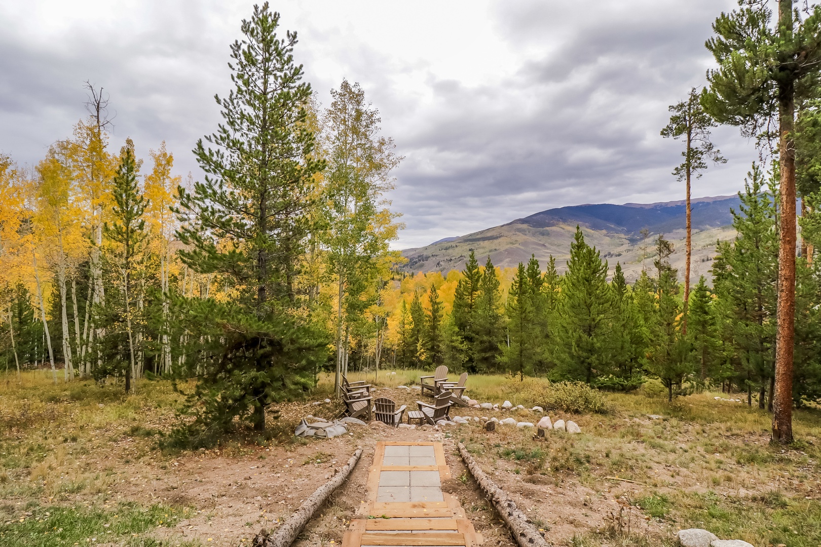An outdoor fire pit area set within forested grounds, with distant mountains framing the natural landscape around the property.