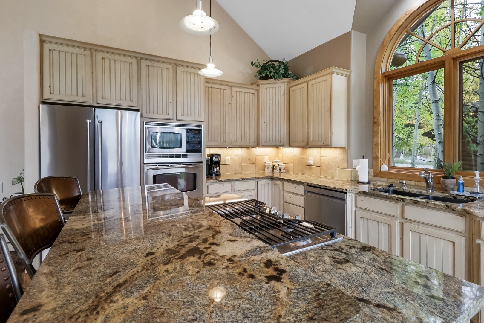 Your gourmet kitchen awaits with gleaming granite countertops, professional-grade gas cooking, and stunning arched windows that frame peaceful forest views while you prepare meals.