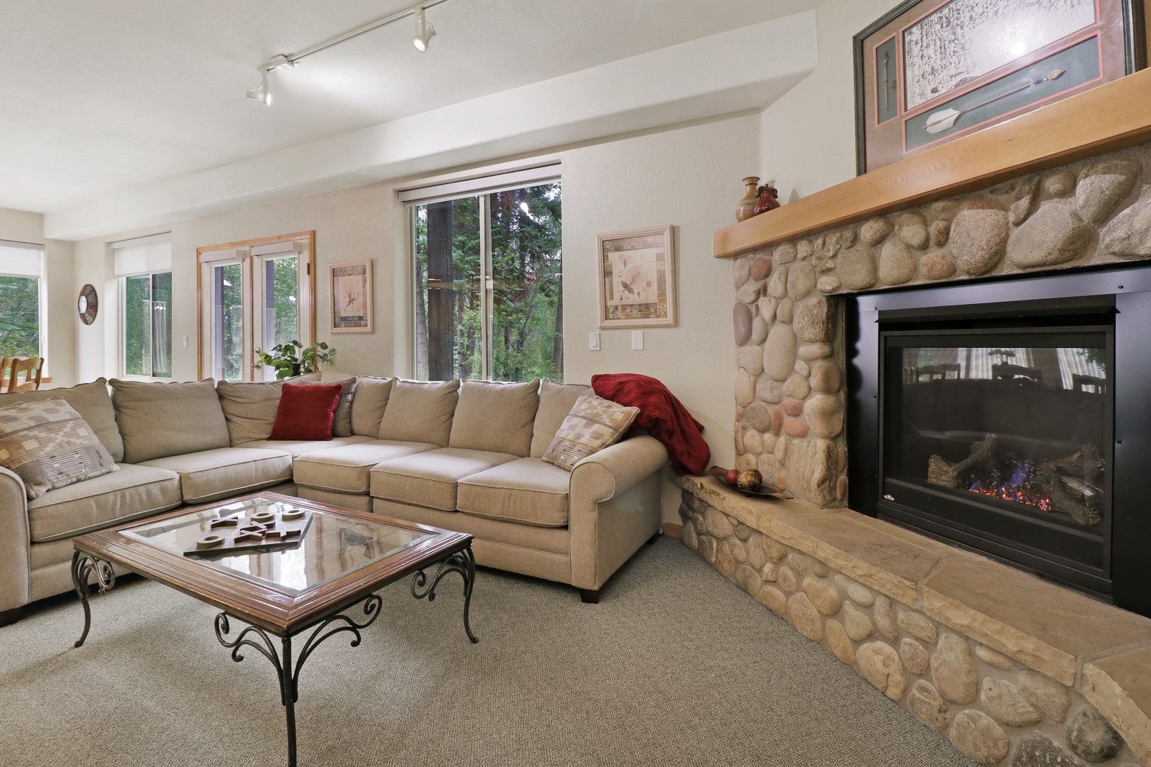 Settle into the inviting living room with a plush sectional and cozy fireplace. Natural light streams through large windows framing peaceful forest views, while the stone hearth adds rustic mountain charm.