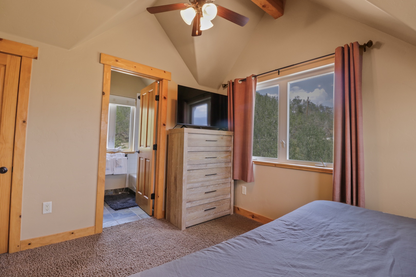 Your restful bedroom features vaulted ceilings, warm wood accents, and large windows framing natural greenery beyond. Enjoy the comfort of thoughtful furnishings and peaceful mountain surroundings.