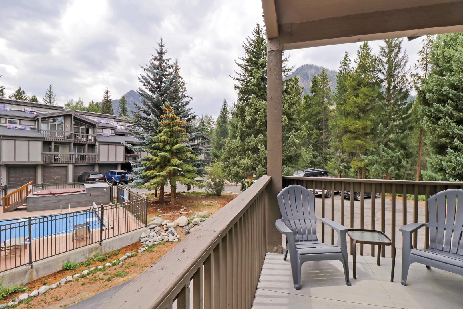 A covered balcony overlooking poolside amenities and mountain scenery framed by tall evergreens. Perfect for your morning coffee or evening relaxation with views of both community and nature.