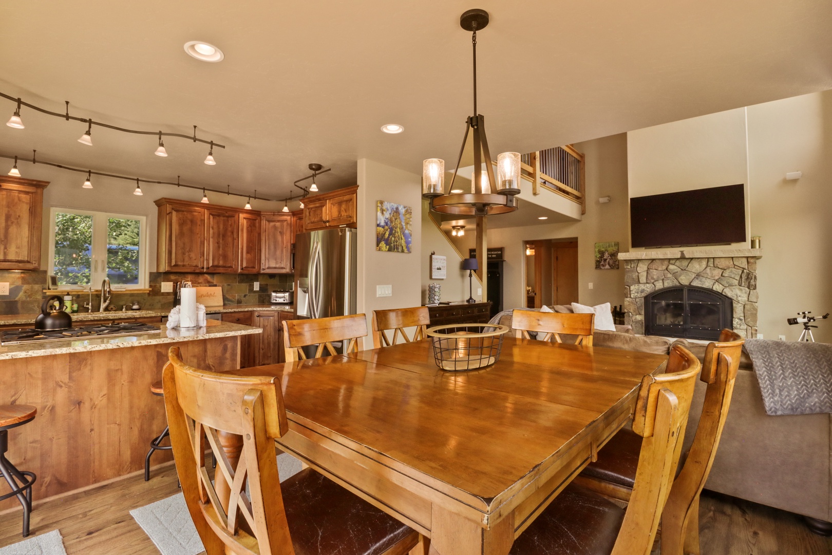 A warm, open-concept space where your family can gather around the stunning wood dining table, cook together in the fully-equipped kitchen, and unwind by the stone fireplace—all under soaring ceilings and warm lighting.