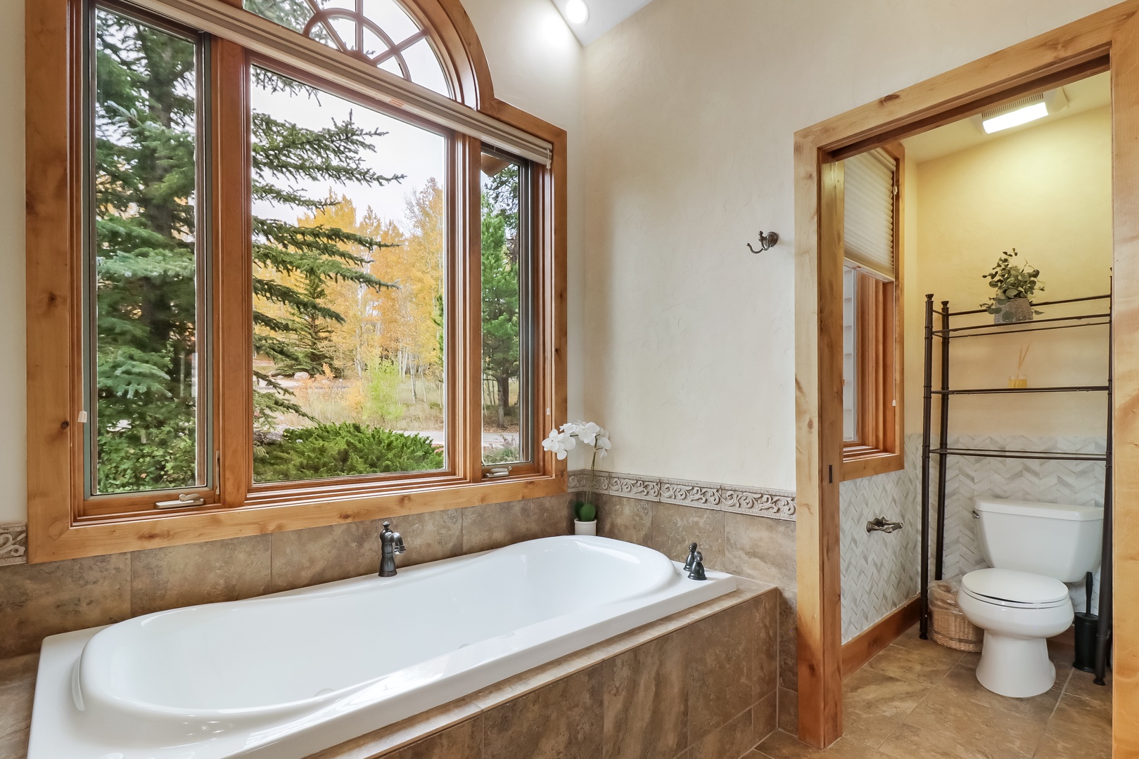 Soak in the elegant soaking tub while natural light pours through soaring arched windows framing peaceful forest views.