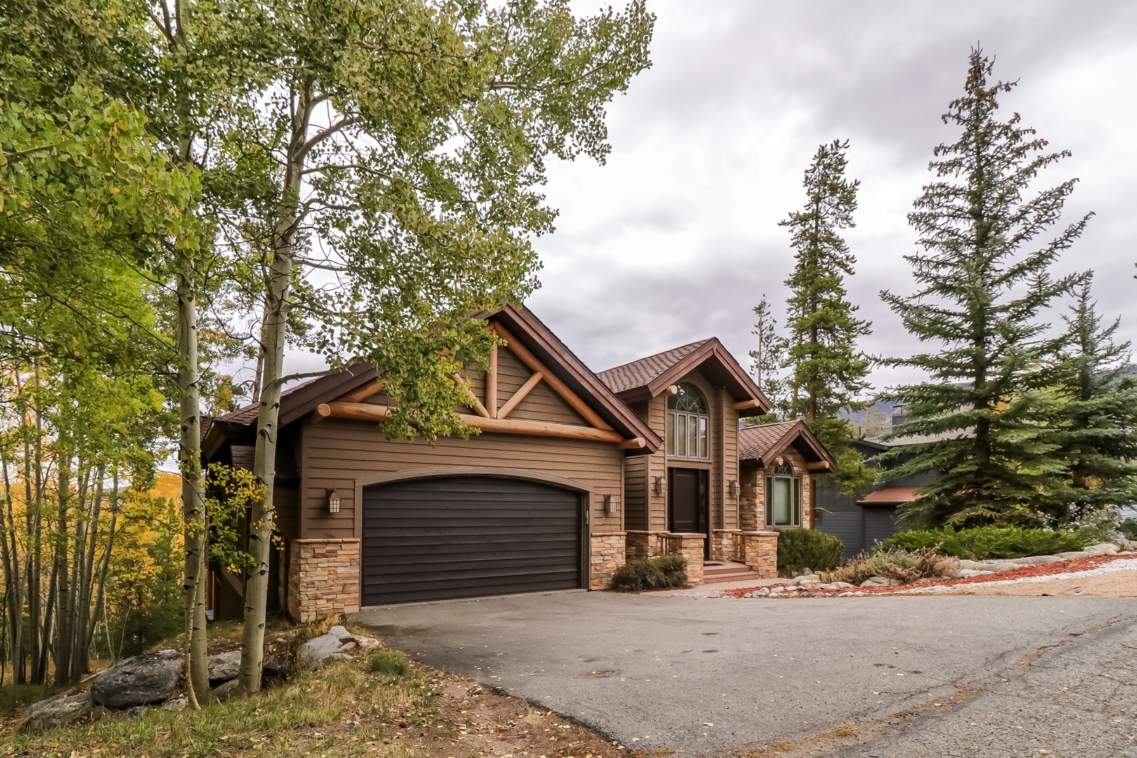 A mountain-style lodge with stone accents and timber detailing, nestled among aspen and pine trees with convenient parking.