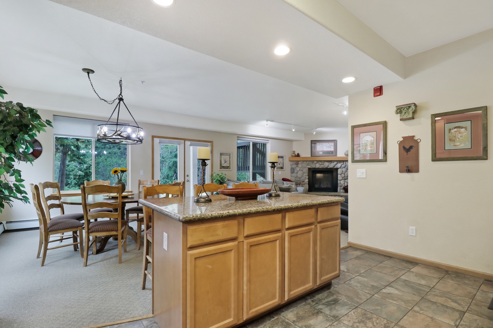 Step into this welcoming open living space where a granite island anchors the kitchen and flows seamlessly into the dining area. Gather around the table or relax by the stone fireplace with views of lush greenery just outside.