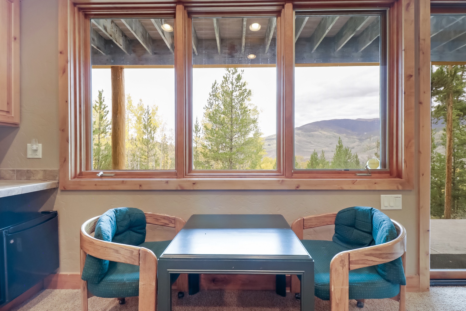 Your dining nook frames a stunning mountain view through expansive windows, where evergreen trees meet distant peaks—perfect for lingering over morning coffee as natural light fills the space.