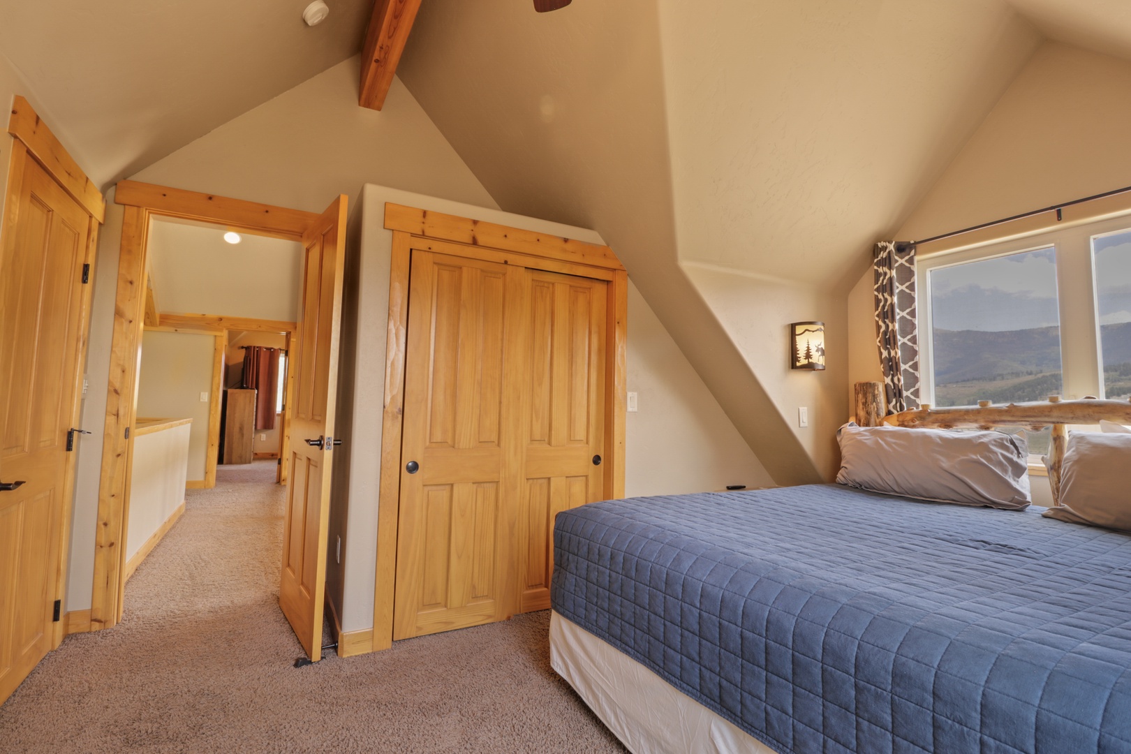 Your peaceful upstairs bedroom features vaulted ceilings, rustic wood beams, and a stunning mountain view through large windows—perfect for waking up to nature's beauty.