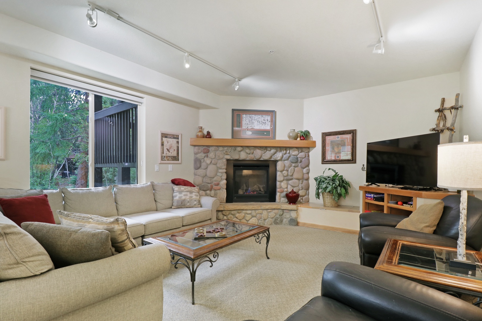 Sink into plush seating around the stone fireplace, where natural light and mountain greenery frame your perfect retreat.