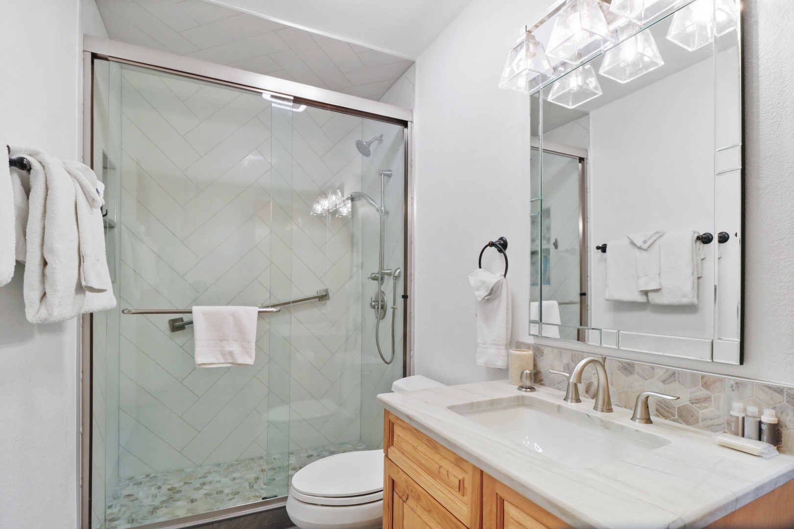 Refresh in your elegant bathroom with herringbone tile shower, marble vanity, and modern lighting creating a spa-like retreat.